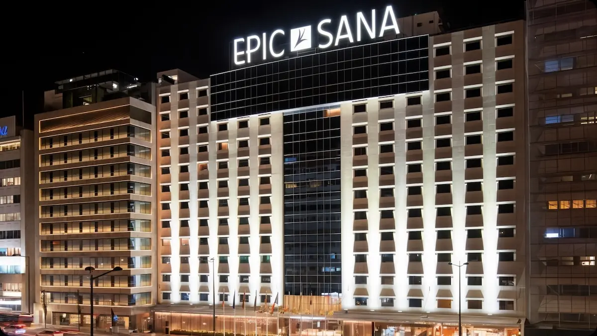 Fachada do hotel EPIC SANA à noite, com iluminação arquitetural vertical e letreiro luminoso no topo do edifício.