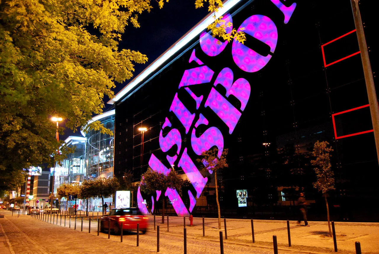 Fachada exterior do Casino Lisboa à noite, com o letreiro projetado em grande escala sobre o edifício, em magenta.
