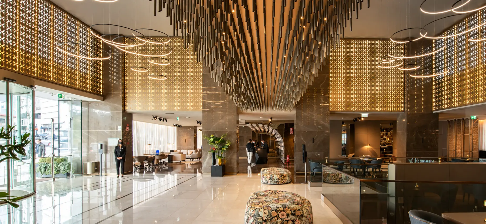 Átrio do hotel SANA Marquês, com painéis retroiluminados, luminárias circulares suspensas e um teto de elementos verticais.