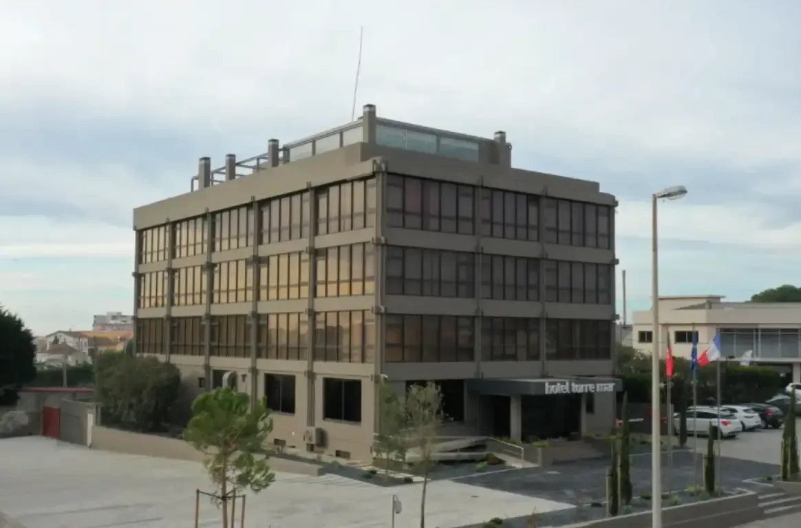 O edifício do hotel, de linhas retas e janelas em banda, visto do estacionamento em frente.
