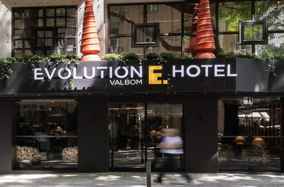 Entrada do hotel, com o letreiro Evolution Valbom Hotel por cima das montras de vidro e peças decorativas vermelhas.