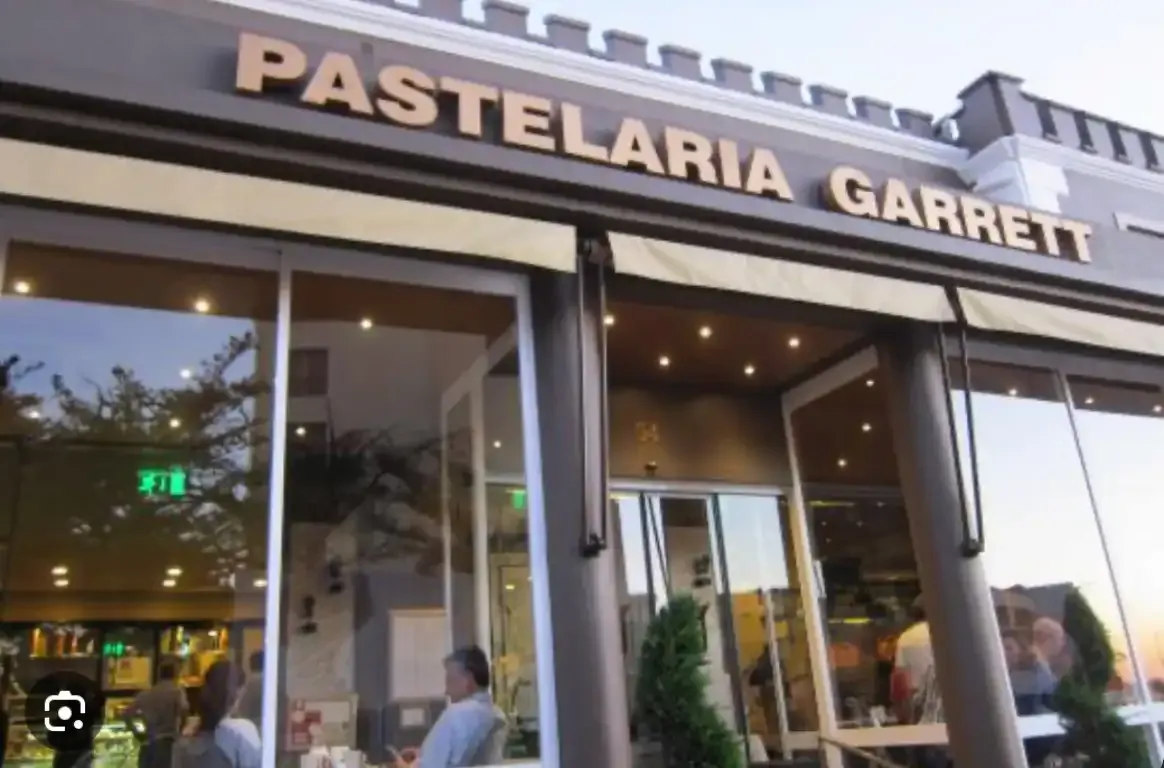 Fachada com o letreiro PASTELARIA GARRETT, toldos e montras envidraçadas, com clientes sentados no interior.