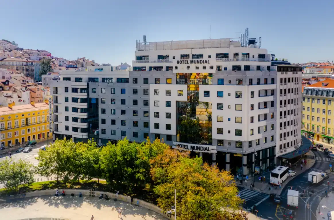 O edifício do hotel visto do alto, entre os telhados da cidade, com árvores e uma praça em primeiro plano.