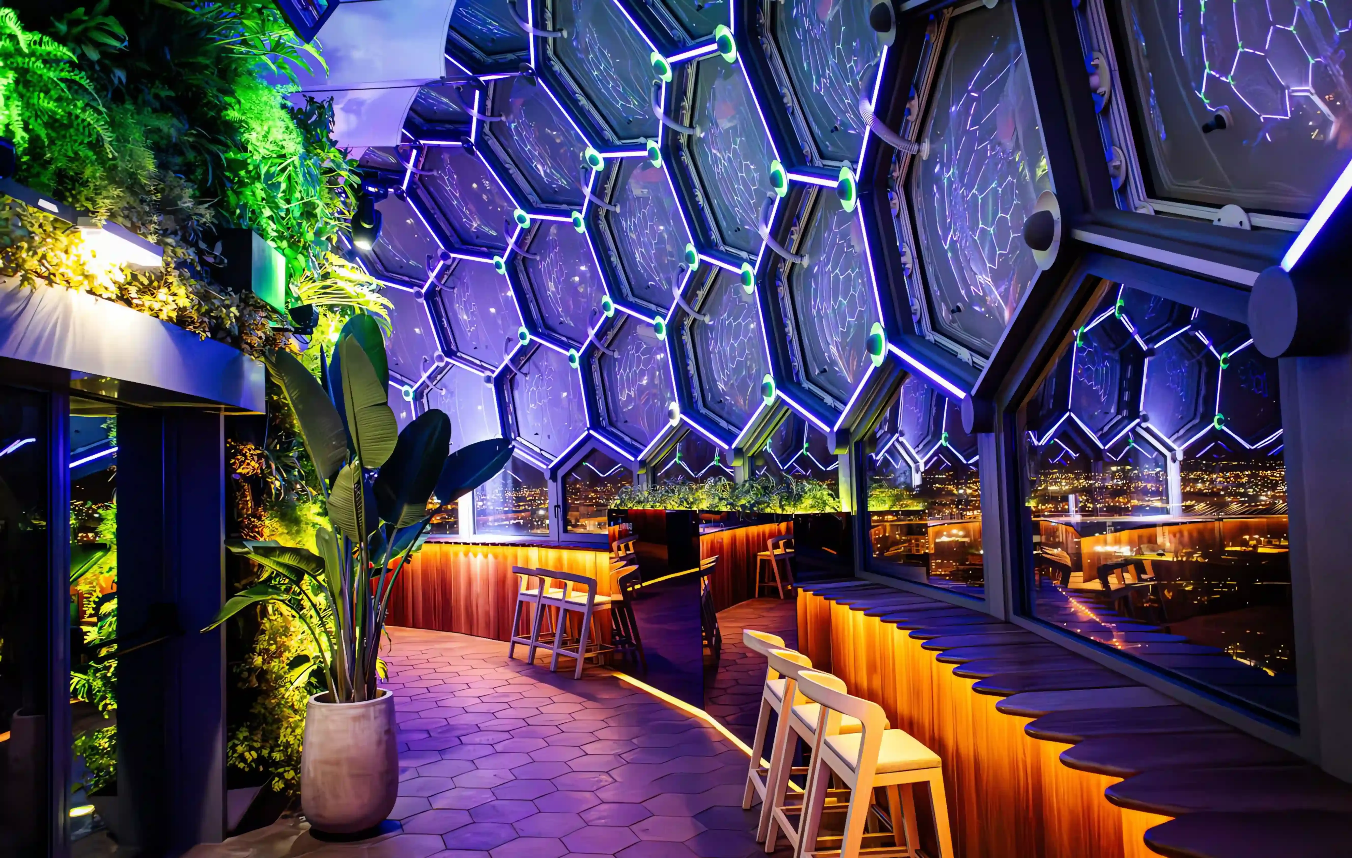 BABYLON 360º: sala do rooftop ao início da noite, com os painéis hexagonais em azul e violeta e a cidade ao fundo.