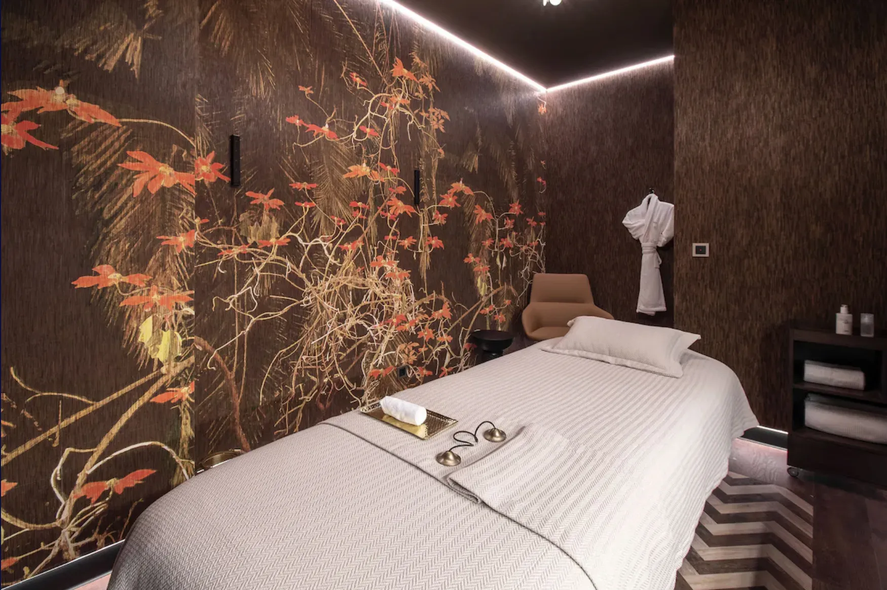 Sala de tratamento do spa com marquesa, parede com motivo floral e iluminação de contorno no teto.