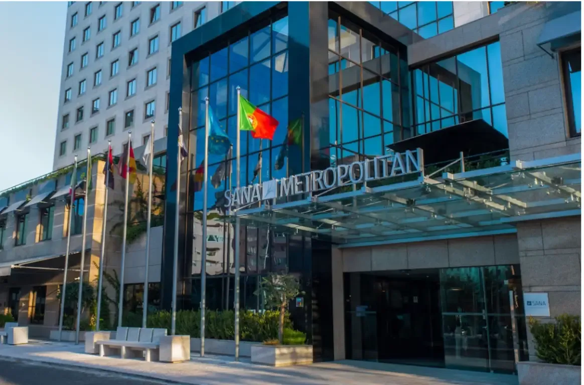 Entrada do hotel, com a pala envidraçada, o letreiro SANA Metropolitan e mastros com bandeiras.