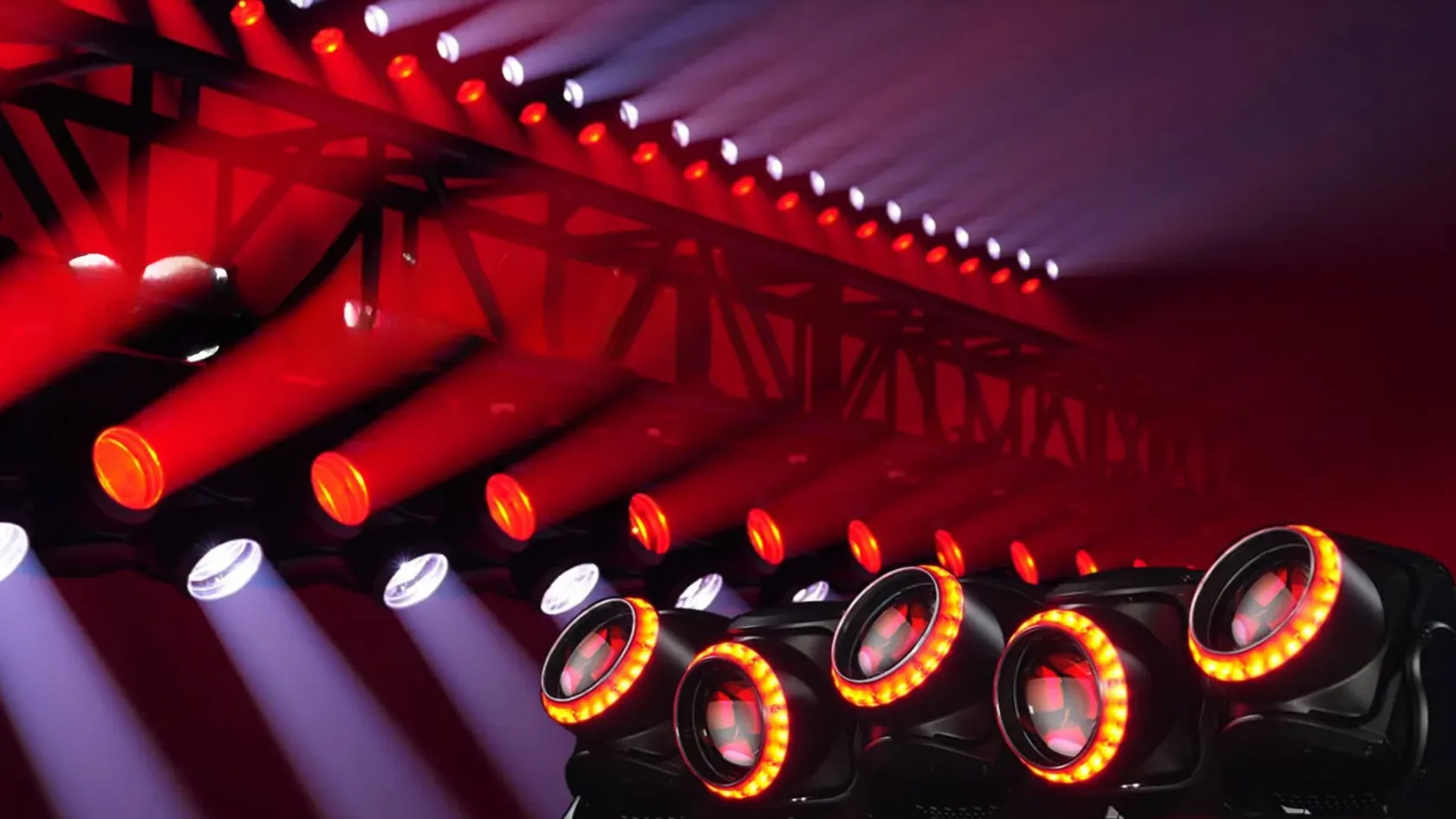 Ponte de treliça com dezenas de projetores a lançar feixes vermelhos e brancos, e cinco cabeças móveis com aros de LED cor de laranja em primeiro plano.
