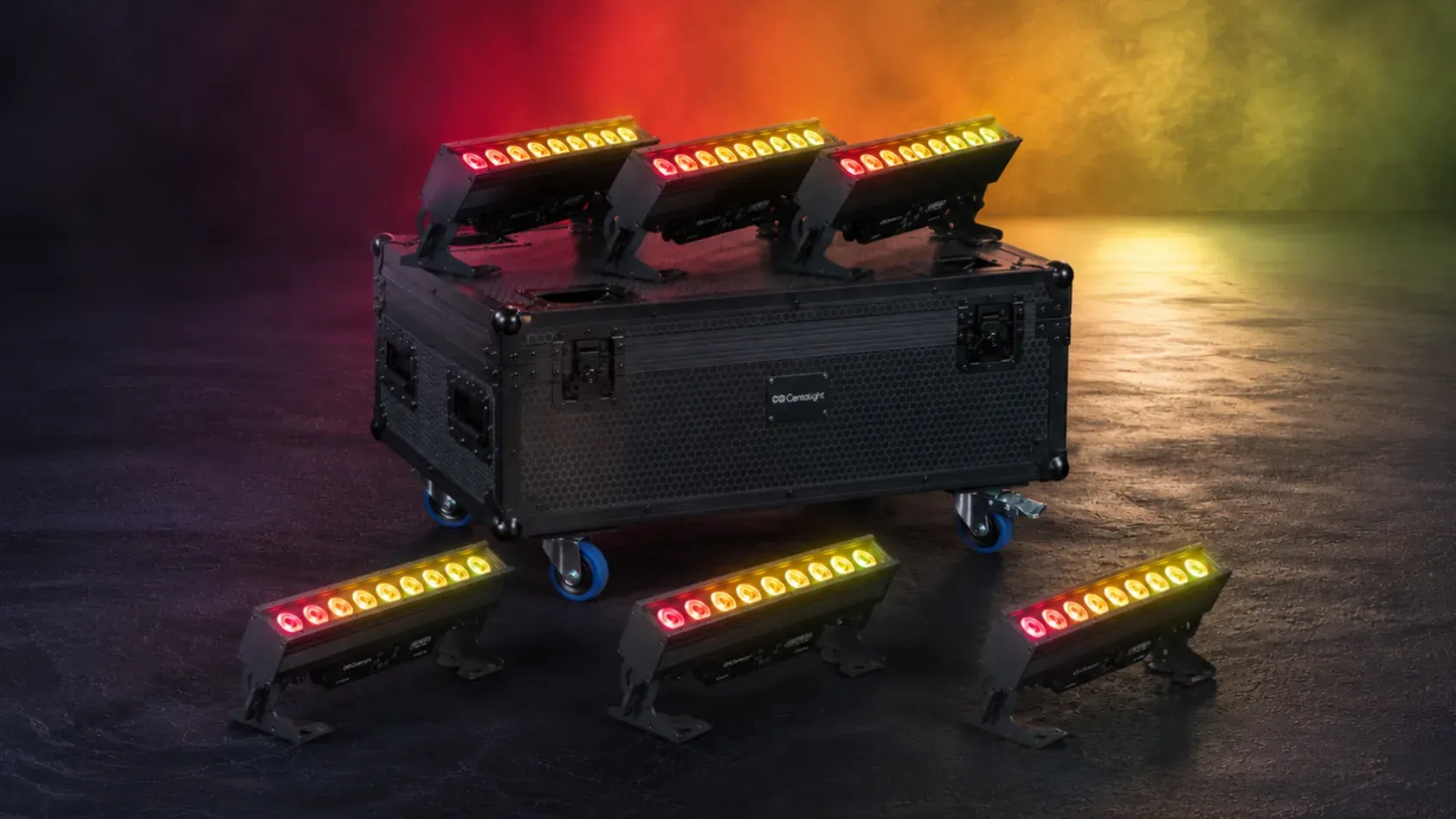 Seis barras de LED acesas em vermelho, laranja e amarelo, três pousadas sobre uma mala de transporte preta e três no chão, num estúdio escuro.