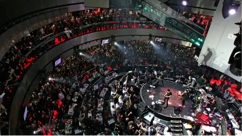 Sala de espetáculos do Casino Lisboa durante um concerto, vista de cima, com o público em redor do palco central.